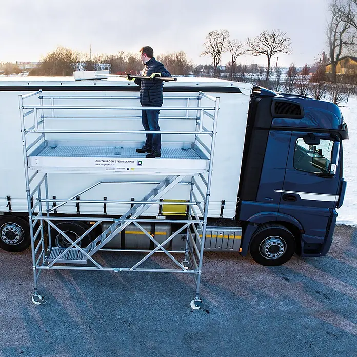 Munk Plattformgerüst Mobiles Enteisungsgerüst 70500 -  - Mobiles Gerüst aus silbernem Aluminium, das ein Mann zum Schneeräumen vom LKW-Dach nutzt.
