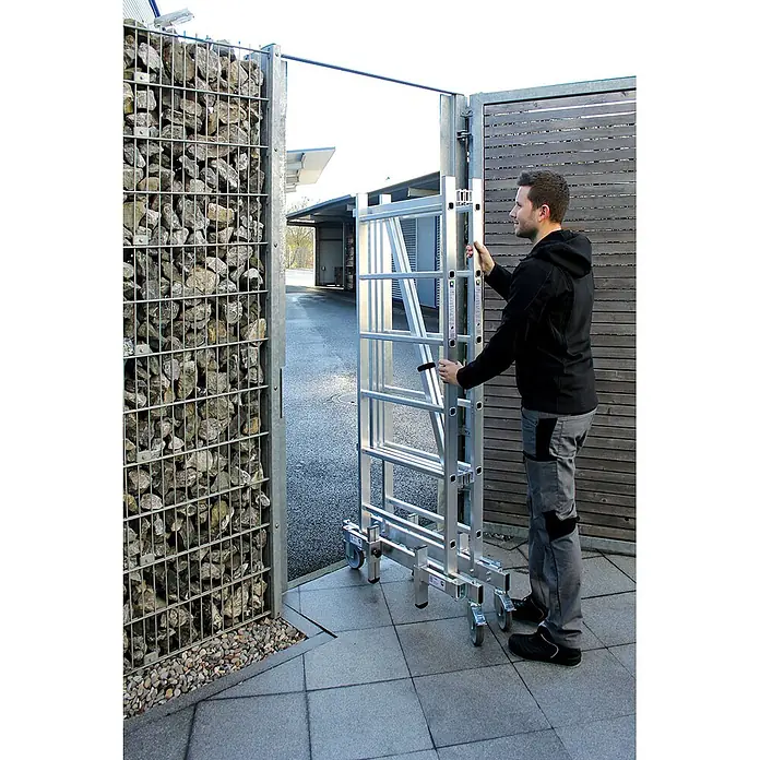 Munk Rollgerüst ML Rollgerüst 3m AH mit Teleskopauslegern - Arbeitshöhe: 3.000 m - Mann schiebt ein leichtes mobiles Aluminium-Rollgerüst auf Rädern durch ein Außentor.