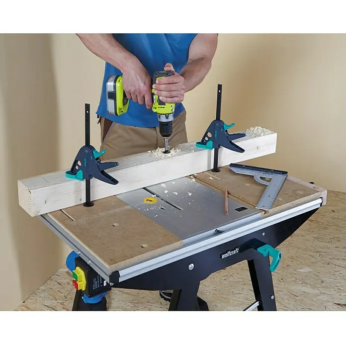 Wolfcraft Sargento 65-150-W - Anchura de sujeción: 120 mm - Un banco de trabajo Wolfcraft con una persona taladrando una pieza de madera sujetada con abrazaderas.