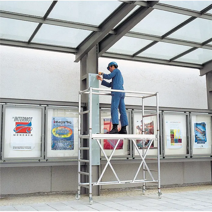 Iller Leiter Rollgerüst Professional Klappgerüst mit Ausbaueinheit 1,35x1,80 m | 3,50m AH - Arbeitshöhe: 3.500 m - Aluminium-Rollgerüst mit Arbeiter bei Installationsarbeiten unter einem Glasdach.