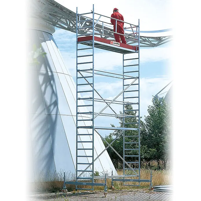 Euroline Rollgerüst Gerüst 9516 mit Sicherheitsaufbau und Auslegern 3,35m AH - Arbeitshöhe: 3.350 m - Mobiles Rollgerüst aus silbernem Metall mit roter Plattform. Ein Arbeiter in Rot steht oben und führt Arbeiten im Freien aus.