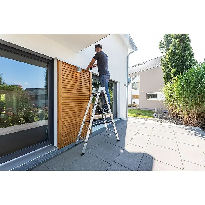 Munk Doppel-Stehleiter Sprossenstehleiter 2x10 Sprossen - Anzahl Tritte: 10 Stk., Arbeitshöhe: 4.200 m, Aluminium - Silberne Aluminium-Klappleiter mit Holzstufen, von einem Mann zur Arbeit an einer Hauswand genutzt.