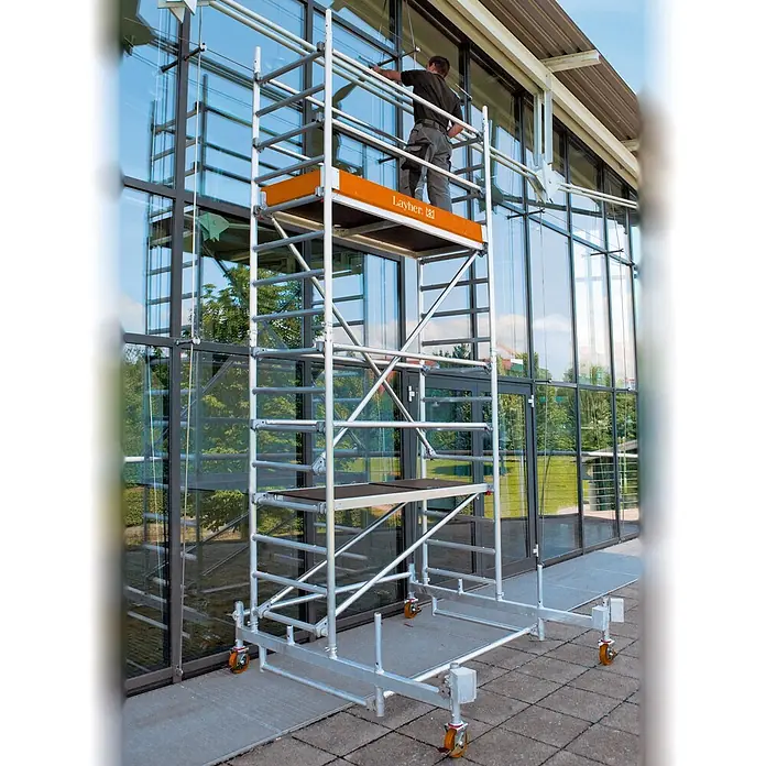 Layher Rollgerüst Rollgerüst Uni Leicht 9,26m AH - Arbeitshöhe: 9.260 m - Mobiles Gerüst aus silbernem Aluminium, Person reinigt Fenster eines modernen Gebäudes.