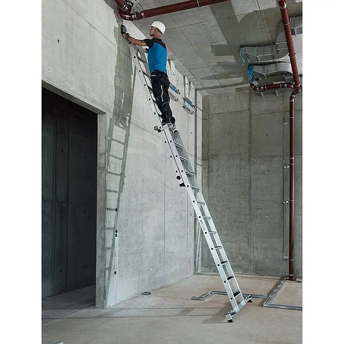 Munk Schiebeleiter Stufen-Schiebeleiter mit nivello-Traverse 2-teilig 14+10 Stufen - Anzahl Tritte: 14 Stk., Arbeitshöhe: 6.200 m, Aluminium - Arbeiter auf einer silbernen, verstellbaren Aluminiumleiter, sicher auf Betonboden positioniert, bei Wandinstallationen.