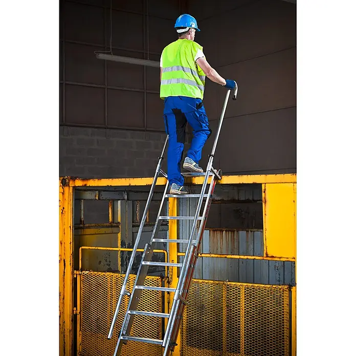 Hymer Schiebeleiter Einhängeleiter Schiebeleiter Regaleinhängeleiter 2x8 Sprossen - Arbeitshöhe: 4.950 m, Aluminium - Eine Person in Arbeitsschutzkleidung steigt eine silberne Aluminiumleiter mit Handläufen hinauf, um eine erhöhte Industriestruktur zu erreichen.