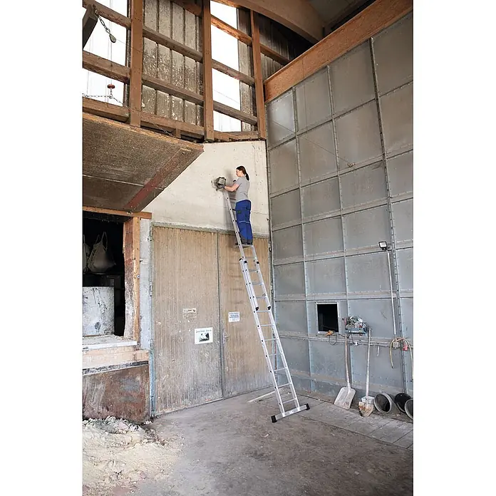 Munk Schiebeleiter Schiebeleiter 2x6 Sprossen - Anzahl Tritte: 6 Stk., Arbeitshöhe: 4.100 m, Aluminium - Aluminium-Mehrzweckleiter, von einer Frau zum Arbeiten an einer Wand benutzt.