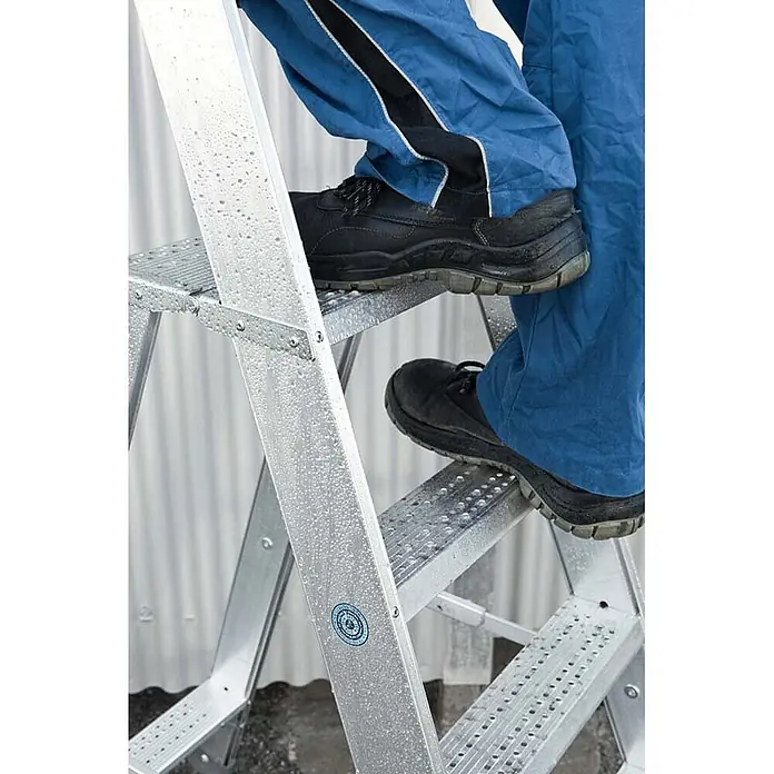 Zarges Stehleiter Stehleiter Seventec RC 4 Stufen - Anzahl Tritte: 4 Stk., Arbeitshöhe: 2.900 m, Aluminium - Person in blauer Arbeitskleidung steigt eine nasse silberne Metallleiter hinauf.