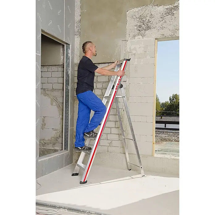 Hymer Stehleiter Stufenstehleiter mit Plattform 8 Stufen - Anzahl Tritte: 8 Stk., Arbeitshöhe: 3.840 m, Aluminium - Silberne Aluminium-Stehleiter mit roten Akzenten, die von einem Mann auf einer Baustelle verwendet wird.