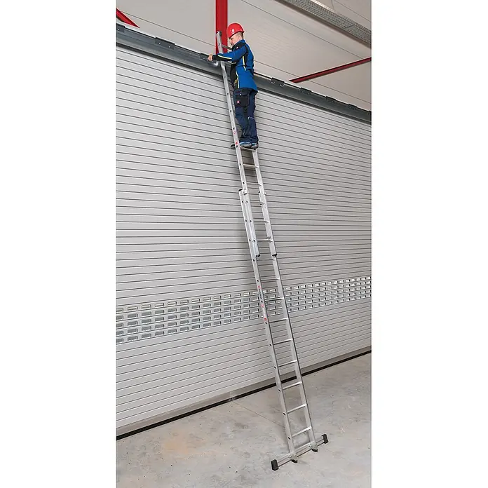 Euroline Schiebeleiter Premium 302 Schiebeleiter 2x18 Sprossen - Anzahl Tritte: 18 Stk., Arbeitshöhe: 10.600 m, Aluminium - Silberne Aluminium-Anlegeleiter, von einem Arbeiter an einer hohen Industrietür verwendet.