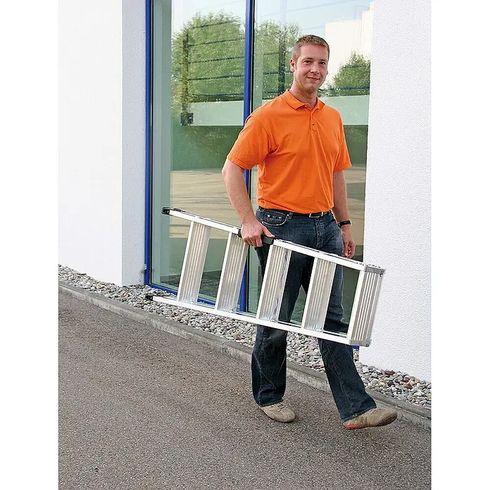 Munk Stehleiter Stehleiter beidseitig begehbar mit relax-step 2x14 Stufen - Anzahl Tritte: 6 Stk., Arbeitshöhe: 2.900 m, Aluminium - Mann trägt eine silberne Aluminium-Klappleiter, was ihre Portabilität zeigt.