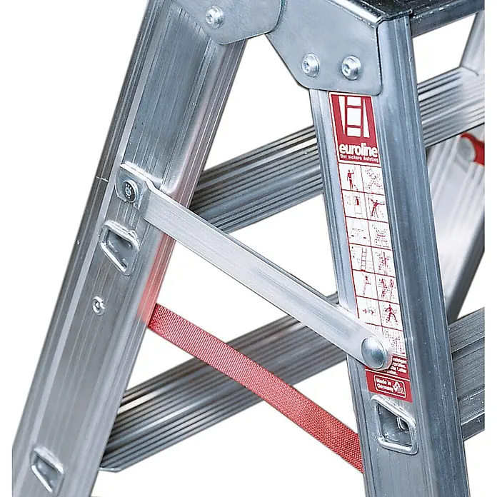 Euroline Stehleiter Premium 30573 Stufenstehleiter mit Federrollen und Feststellern 2x4 Stufen - Anzahl Tritte: 4 Stk., Arbeitshöhe: 2.450 m, Aluminium - Nahaufnahme eines Aluminium-Klappleitergelenks mit rotem Sicherheitsgurt und Sicherheitshinweisetikett.