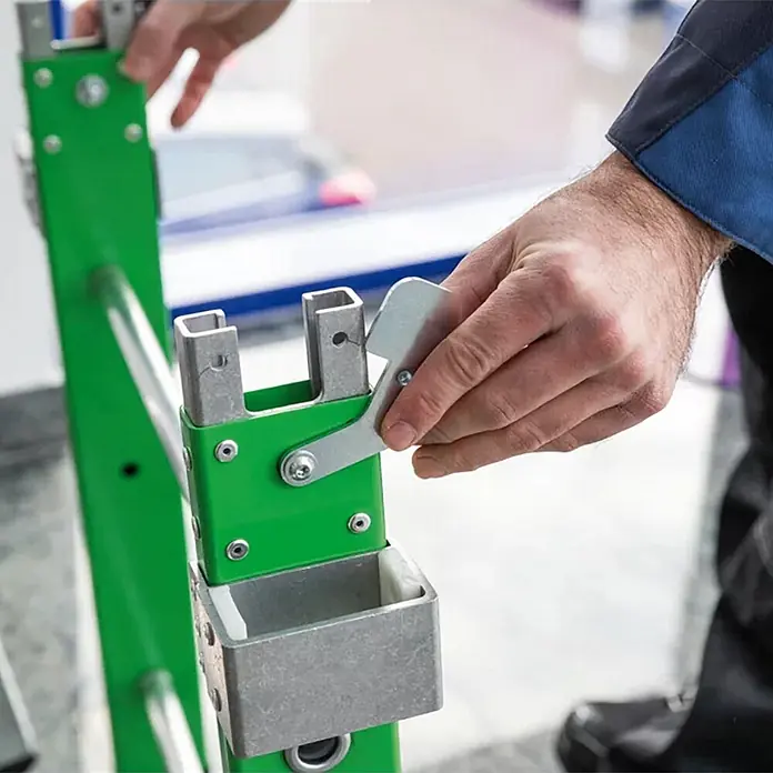 Munk Podestleiter Einsteckteil Plus 4 Stufen für steckbare Plattformleiter - Aluminium - Hände bedienen einen silbernen Metallhebel an einer grünen Rahmenhalterung mit kleinem Behälter.