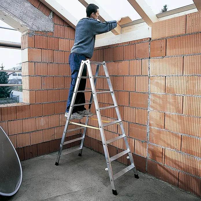 Zarges Stehleiter gebördelte Doppelstufenleiter Nova B 2x5 Stufen - Anzahl Tritte: 5 Stk., Arbeitshöhe: 2.550 m, Aluminium - Aluminium-Klappleiter im Einsatz auf einer Baustelle, ein Mann steht darauf, um Dachsparren zu erreichen.