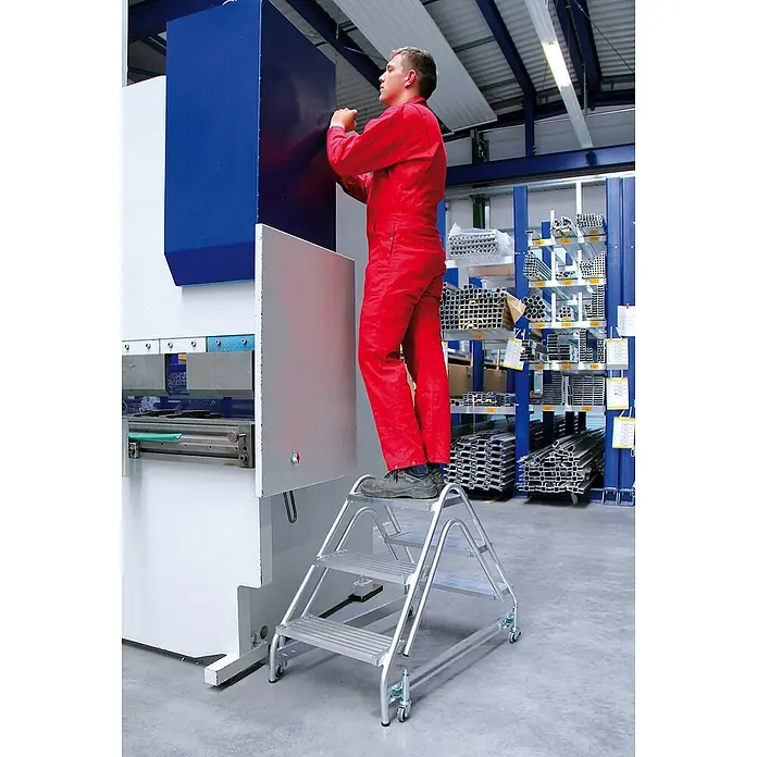 Munk Stehleiter Aluminium Arbeitspodest 2x4 Stufen - Anzahl Tritte: 4 Stk., Arbeitshöhe: 3.000 m, Aluminium - Silberne Aluminium-Trittleiter mit Rollen, von einem Arbeiter an einer Maschine genutzt.