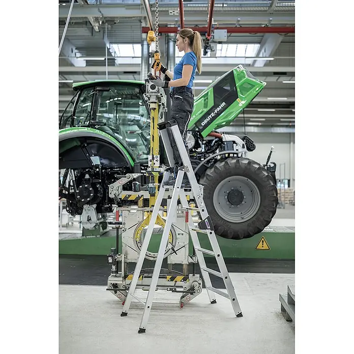Munk Stehleiter Stehleiter mit clip-step 5 Stufen - Anzahl Tritte: 5 Stk., Arbeitshöhe: 3.150 m, Aluminium - Silberne Aluminium-Stehleiter, von einer Frau bei der Arbeit an einem Traktor in einer Fabrik genutzt. Bietet sicheren Stand.
