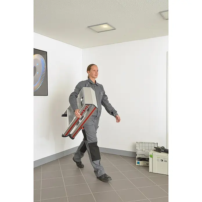 Hymer Stehleiter Stufenstehleiter mit vernieteten Leiterschuhen 2x8 Stufen - Anzahl Tritte: 8 Stk., Arbeitshöhe: 3.370 m, Aluminium - Frau in grauer Arbeitskleidung trägt eine zusammengeklappte silberne HYMER Leiter mit roten Akzenten, zeigt ihre Portabilität.