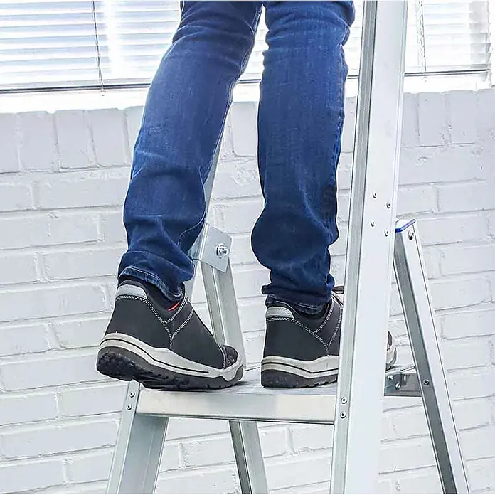 ASC Stehleiter Eurostairs Stufenstehleiter einseitig eloxiert mit Plattform 4 Stufen - Anzahl Tritte: 4 Stk., Arbeitshöhe: 2.800 m, Aluminium - Person in Jeans und Schuhen steigt eine silberne Aluminiumleiter hoch.
