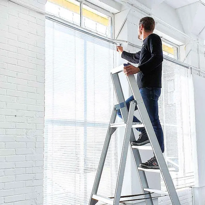 ASC Stehleiter Eurostairs Stufenstehleiter einseitig eloxiert mit Plattform 4 Stufen - Anzahl Tritte: 4 Stk., Arbeitshöhe: 2.800 m, Aluminium - Silberne Aluminium-Klappleiter in Gebrauch, ein Mann erreicht damit Fensterjalousien.