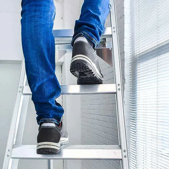 ASC Stehleiter Eurostairs Stufenstehleiter einseitig eloxiert mit Plattform 4 Stufen - Anzahl Tritte: 4 Stk., Arbeitshöhe: 2.800 m, Aluminium - Person in Arbeitsschuhen klettert eine silberne Aluminiumleiter hoch.