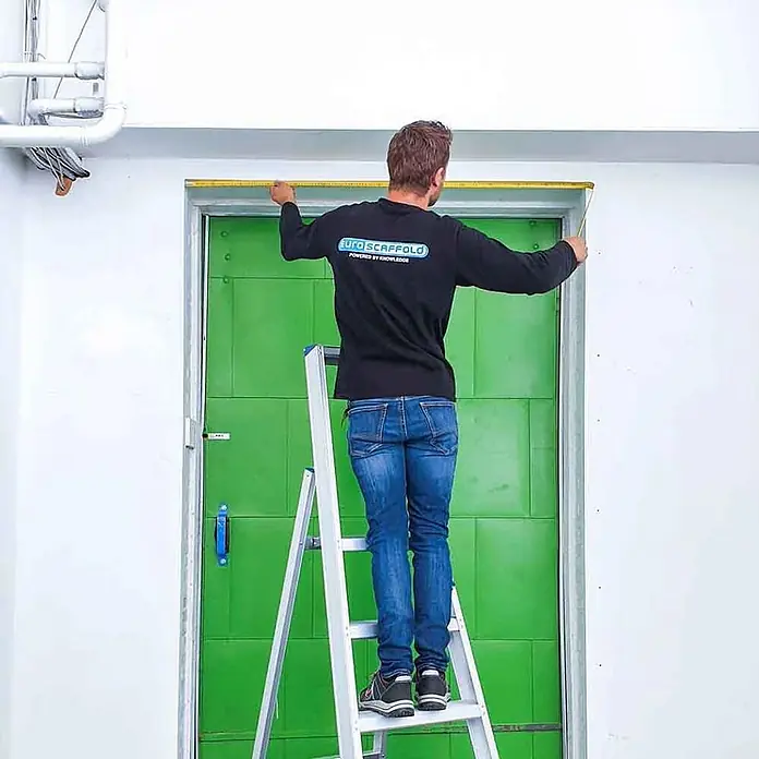 ASC Stehleiter Eurostairs Stufenstehleiter einseitig eloxiert mit Plattform 4 Stufen - Anzahl Tritte: 4 Stk., Arbeitshöhe: 2.800 m, Aluminium - Mann auf einer silbernen Stehleiter misst einen Türrahmen.