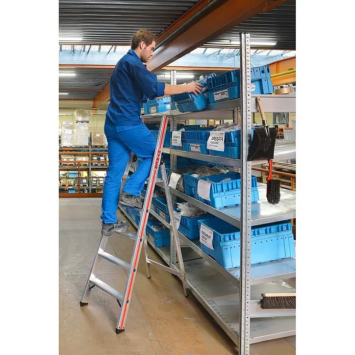 Hymer Stehleiter Stufenstehleiter mit Plattform und Aluminium Ablageschale 7 Stufen - Anzahl Tritte: 7 Stk., Arbeitshöhe: 3.630 m, Aluminium - Ein Mann benutzt eine silberne HYMER Leiter, um Gegenstände in einem Lagerregal zu erreichen.