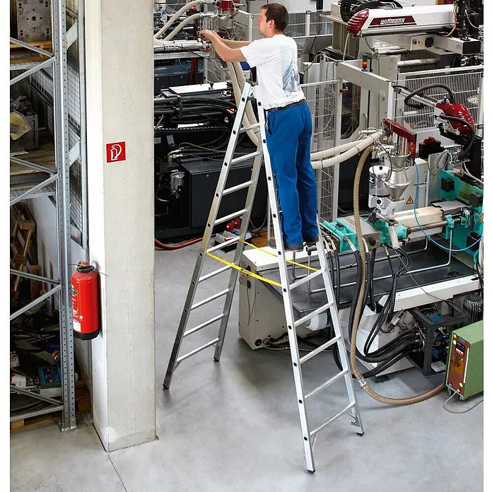 Zarges Stehleiter Sprossenstehleiter Coni B 2x18 Sprossen - Anzahl Tritte: 18 Stk., Arbeitshöhe: 6.150 m, Aluminium - Mann auf einer silbernen Doppelleiter mit gelbem Sicherheitsgurt, arbeitet an Industriemaschinen.