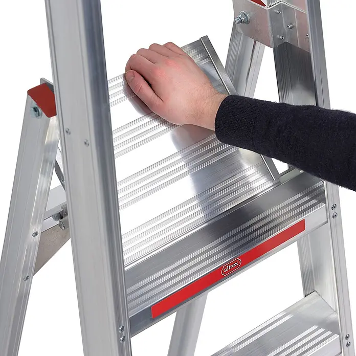 Altrex Stehleiter Sierra Stufenstehleiter SEO 5 Stufen - Anzahl Tritte: 5 Stk., Arbeitshöhe: 3.200 m - Eine Hand drückt auf die gerippte, rutschfeste Plattform einer silbernen Aluminium-Stehleiter mit roten Akzenten.