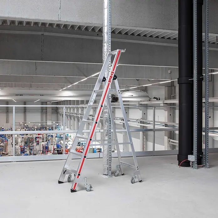 Hymer Stehleiter Stufenstehleiter mit Plattform und Rollen 6 Stufen - Anzahl Tritte: 6 Stk., Arbeitshöhe: 3.400 m, Aluminium - Silberne Aluminiumleiter mit roten Akzenten und Rollen, stehend in einer großen Industriehalle.