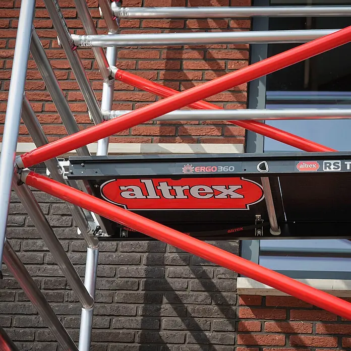 Altrex Rollgerüst Fahrgerüst RS Tower 52 Aluminium mit Fiber-Deck Plattform 13,20m AH 1,35x2 - Arbeitshöhe: 13.200 m - Gerüstgestell aus rotem und silbernem Aluminium mit schwarzer Plattform vor einer Ziegelwand.