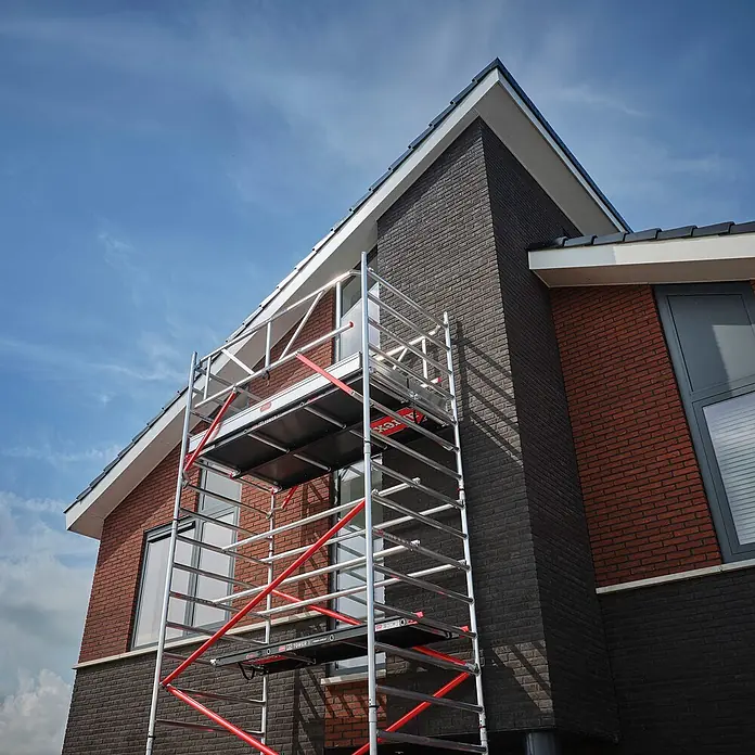 Altrex Rollgerüst Fahrgerüst RS Tower 52 Aluminium mit Fiber-Deck Plattform 13,20m AH 1,35x2 - Arbeitshöhe: 13.200 m - Silber-rotes Fahrgerüst an modernem Backsteinhaus, das bis zur Dachlinie reicht.