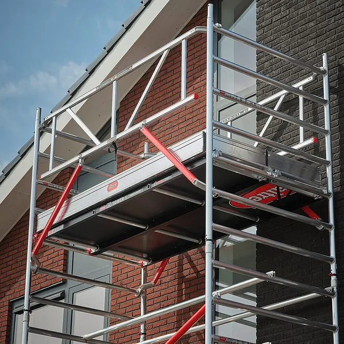 Altrex Rollgerüst Fahrgerüst RS Tower 52 Aluminium mit Fiber-Deck Plattform 13,20m AH 1,35x2 - Arbeitshöhe: 13.200 m - Aluminium-Gerüst mit roten Akzenten an einem Backsteingebäude für Bau- oder Wartungsarbeiten.
