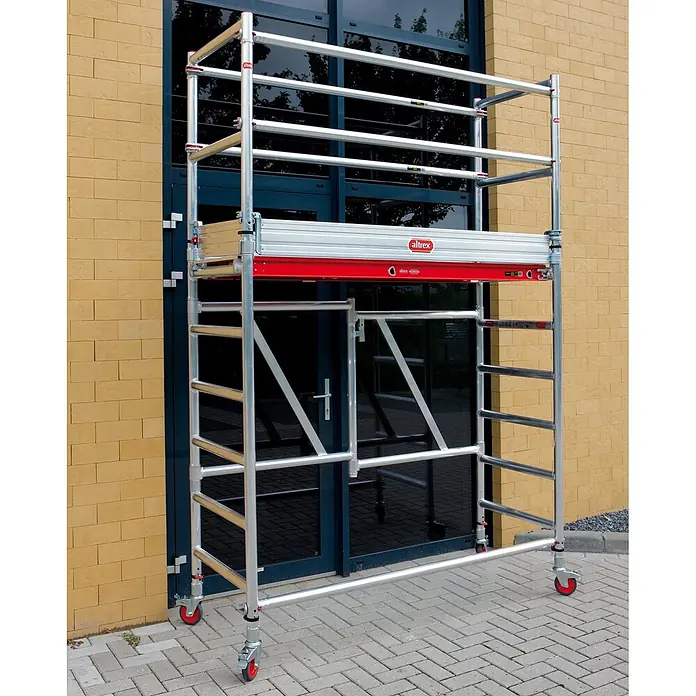 Altrex Rollgerüst Klappgerüst RS Tower 54 Alu Holz-Plattform 0,75x1,85m mit Safe-Quick 8,8m - Arbeitshöhe: 8.800 m - Mobiles Aluminium-Rollgerüst in Silber mit roten Akzenten, im Freien vor einem Gebäude positioniert.