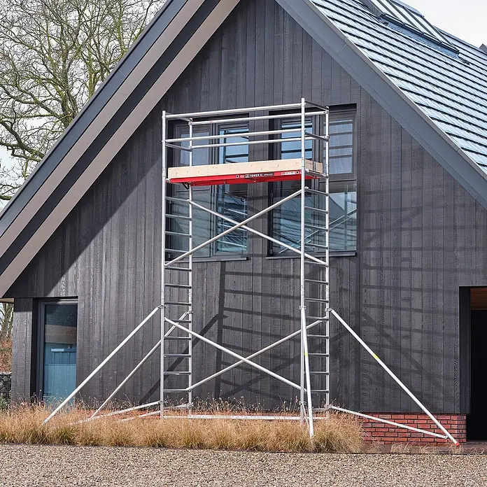 Altrex Rollgerüst Fahrgerüst RS Tower 41 PLUS Aluminium ohne Safe-Quick® mit Holz-Plattform - Arbeitshöhe: 8.200 m - Silbernes Aluminium-Rollgerüst mit roter Plattform, vor einem dunklen Haus aufgestellt.