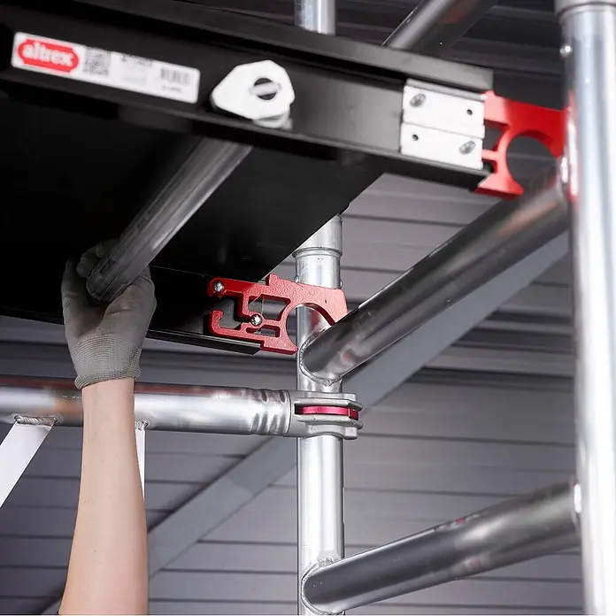 Altrex Rollgerüst MiTower 1-Personen-Gerüst Aluminium mit Holz-Plattform 0,75x1,27m 5,20m AH - Arbeitshöhe: 5.200 m - Mit Handschuh montierte schwarze Gerüstplattform mit roten und silbernen Klemmen auf silbernen Gerüstrohren.