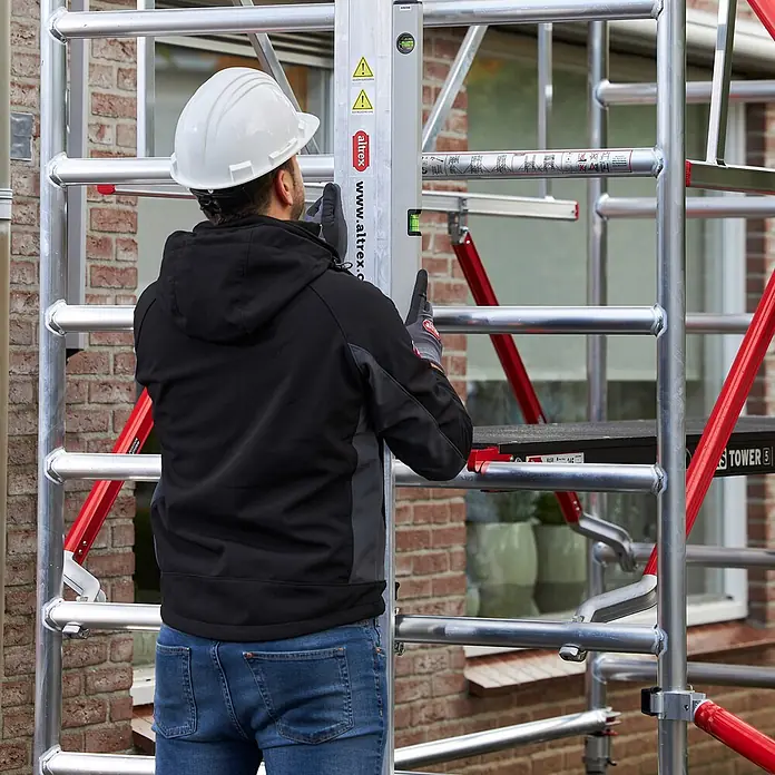 Altrex Rollgerüst Shuttle Basisset mit Winde 3,20m Plattformhöhe 5,20m Arbeitshöhe (kein Ge (Arbeitshöhe: 5.200 m, Belastbarkeit Plattform: 30 kg) -  - Arbeiter nivelliert ein silbernes Aluminiumgerüst.