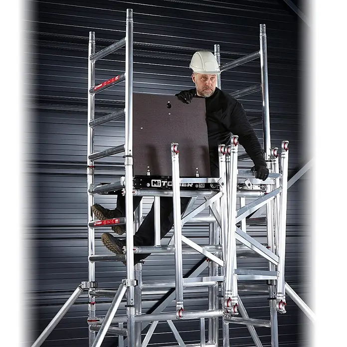 Altrex Rollgerüst MiTower 1-Personen-Gerüst Aluminium mit Holz-Plattform 0,75x1,27m 5,20m AH - Arbeitshöhe: 5.200 m - Mann auf silbernem Aluminium-Rollgerüst, hält dunkle Plattformplatte.