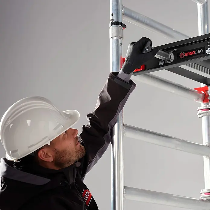 Altrex Rollgerüst MiTower 1-Personen-Gerüst Aluminium mit Holz-Plattform 0,75x1,27m 5,20m AH - Arbeitshöhe: 5.200 m - Arbeiter in Schutzhelm und Handschuhen montiert eine schwarze ERGO360 Gerüstplattform an ein Aluminiumgestell.