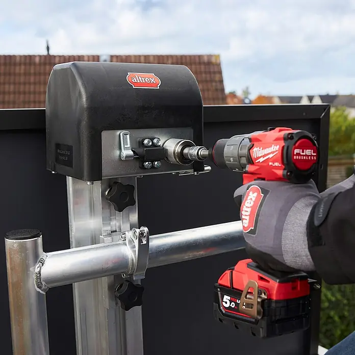 Altrex Rollgerüst Shuttle Basisset mit Winde 3,20m Plattformhöhe 5,20m Arbeitshöhe (kein Ge (Arbeitshöhe: 5.200 m, Belastbarkeit Plattform: 30 kg) -  - Eine Person bedient mit einem roten Milwaukee Bohrer einen schwarzen Altrex Hebeapparat (max. 30 kg).