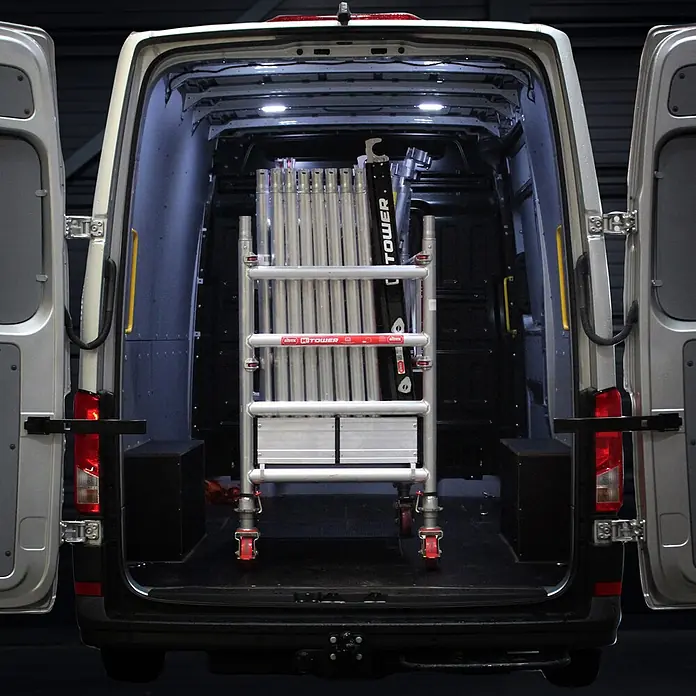 Altrex Rollgerüst MiTower 1-Personen-Gerüst Aluminium mit Holz-Plattform 0,75x1,27m 5,20m AH - Arbeitshöhe: 5.200 m - Geklapptes Aluminium-Rollgerüst mit roten Rollen, im Heck eines weißen Transporters verstaut.