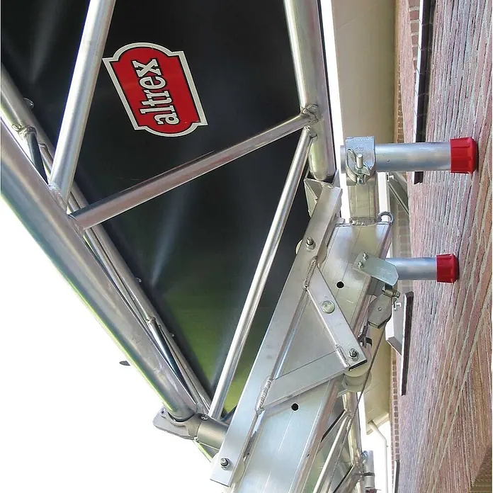 Altrex Rollgerüst Modulare Dreiecksbühne Euro 3-5 mit Handwinde MTB 6m lang -  - Altrex Aluminiumgerüst, schwarze Plattform, rote Endkappen, an einer Ziegelwand montiert.