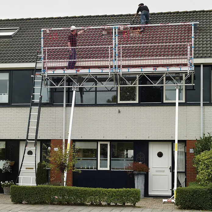 Altrex Rollgerüst Modulare Dreiecksbühne Absturzsicherung mit Fangnetzen für geneigte Däch -  - Aluminiumgerüst mit roten Sicherheitsnetzen an einem Haus für Dacharbeiten, mit zwei Arbeitern.