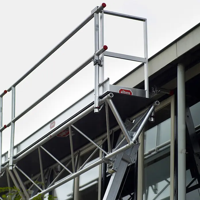 Altrex Rollgerüst Modulare Dreiecksbühne Euro 3-5 mit Handwinde MTB 6m lang -  - Aluminium-Rollgerüst mit Plattform und Schutzgeländer an einem Gebäude.