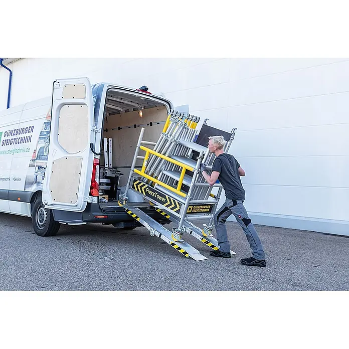 Munk Rollgerüst FlexxTower Ein-Personen-Gerüst 4,10 AH - Arbeitshöhe: 4.100 m - Mann lädt ein silbernes und gelbes FlexxTower Rollgerüst mithilfe einer Laderampe in einen weißen Transporter.