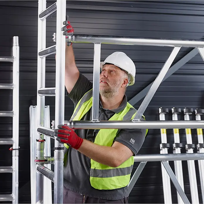 Altrex Rollgerüst MiTower PLUS Fahrgerüst 1-Person-Aufbau Aluminium mit breiter Fiber-Deck P - Arbeitshöhe: 5.200 m - Arbeiter montiert modulares Aluminiumgerüst mit silberfarbenen Bauteilen.