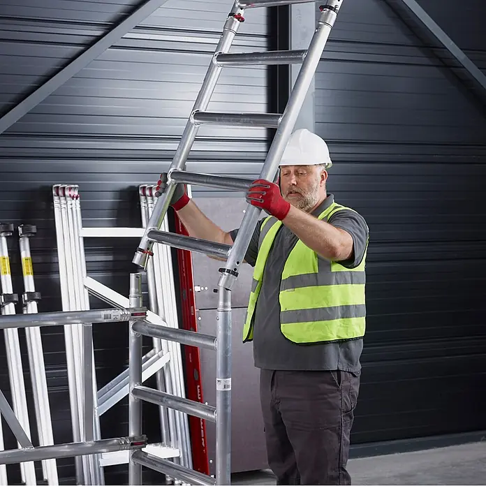 Altrex Rollgerüst MiTower PLUS Fahrgerüst 1-Person-Aufbau Aluminium mit breiter Fiber-Deck P - Arbeitshöhe: 5.200 m - Mann montiert silbernes Aluminium-Gerüst, das sein modulares Design hervorhebt.