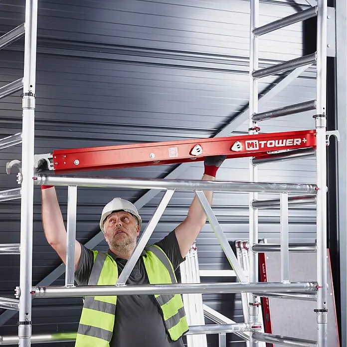 Altrex Rollgerüst MiTower PLUS Fahrgerüst 1-Person-Aufbau Aluminium mit breiter Fiber-Deck P - Arbeitshöhe: 5.200 m - Mann montiert rote MiTOWER+ Gerüstplattform auf Aluminiumgerüst.