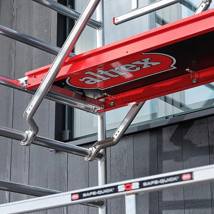 Altrex Rollgerüst Fahrgerüst RS Tower 41-S Aluminium mit Safe-Quick und Holz-Plattform 10,20 - Arbeitshöhe: 10.200 m - Rote Altrex Gerüstplattform und silberne Aluminiumrahmen, Teil eines modulären Gerüstsystems an einem Gebäude.