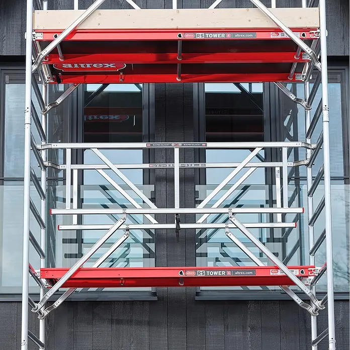 Altrex Rollgerüst Fahrgerüst RS Tower 41-S Aluminium mit Safe-Quick und Holz-Plattform 10,20 - Arbeitshöhe: 10.200 m - Altrex RS TOWER 4 Fahrgerüst mit silbernem Rahmen, roten Plattformen und Holzbohlen vor dunklem Gebäude.