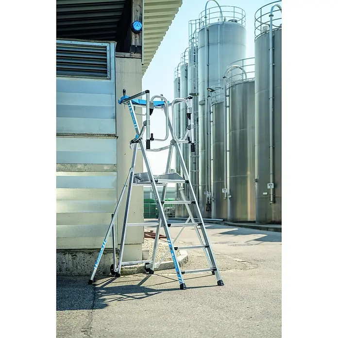 Zarges Teleskopleiter fahrbar gebördelte Teleskop Plattformleiter ZAP SAFEMASTER MAX S 3 Stufen - Anzahl Tritte: 3 Stk., Arbeitshöhe: 2.700 m, Belastbarkeit: 150 kg, Aluminium - Aluminium-Arbeitsplattform mit blauen Akzenten für den Industrieeinsatz, steht im Freien vor Gebäuden und Silos.