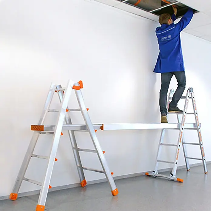Layher Teleskopleiter Topic 1058 Teleskopleiter 4x3 Sprossen - Anzahl Tritte: 3 Stk., Arbeitshöhe: 3.850 m, Aluminium - Silberne Aluminium-Arbeitsplattform mit orangefarbenen Akzenten, wird von einer Person zum Deckenarbeiten genutzt.